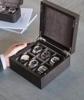 A person holds an open TAWBURY Grove 6 Slot Wooden Watch Box - Kassod Wood - Solid Lid, showcasing six luxury watches elegantly displayed inside.